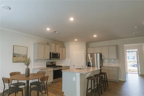 a kitchen with stainless steel appliances granite countertop a stove top oven a refrigerator a kitchen island and chairs with wooden floor