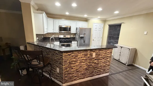 a kitchen with stainless steel appliances kitchen island granite countertop a stove a sink a refrigerator white cabinets and wooden floor