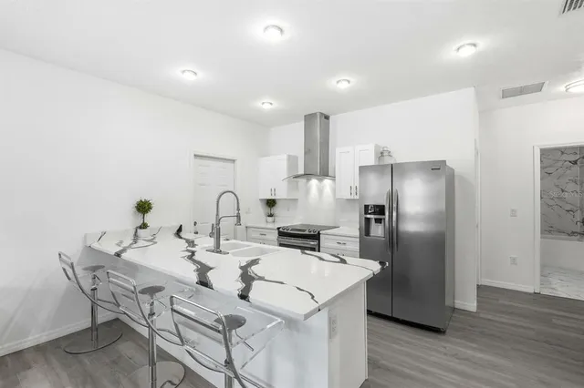 a kitchen with stainless steel appliances kitchen island granite countertop a refrigerator a stove a sink and a dining table with wooden floor