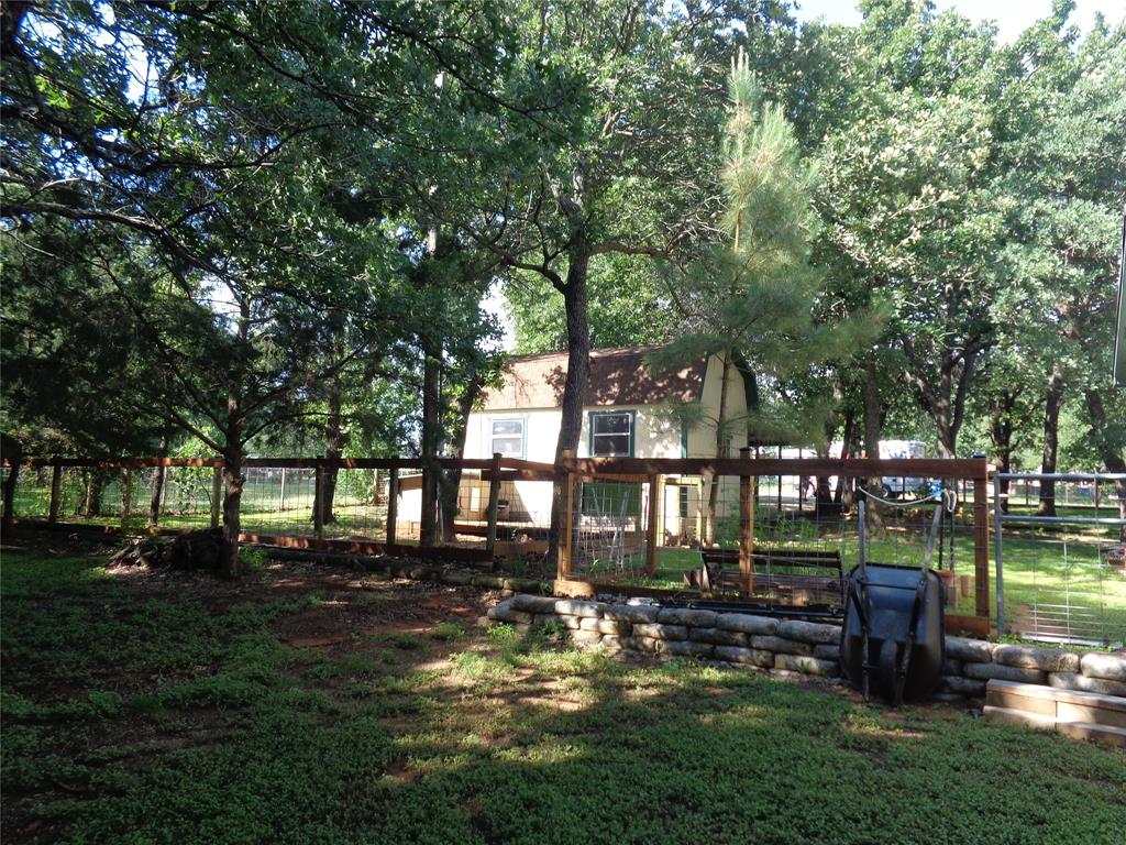 5525 Cedar Oaks Road Grandview, TX 76050 - Photo 8 of 18 Expansive yard featuring mature trees, partial fencing, and a retaining wall