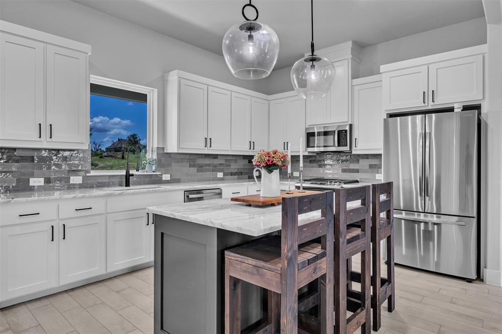 2004 Willy Dilly Road Springtown, TX 76082 - Photo 2 of 40 Kitchen featuring an island with seating, pendant lighting, stainless steel appliances, white cabinetry with dark hardware, and light wood-finish flooring