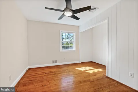 an empty room with wooden floor ceiling fan and window