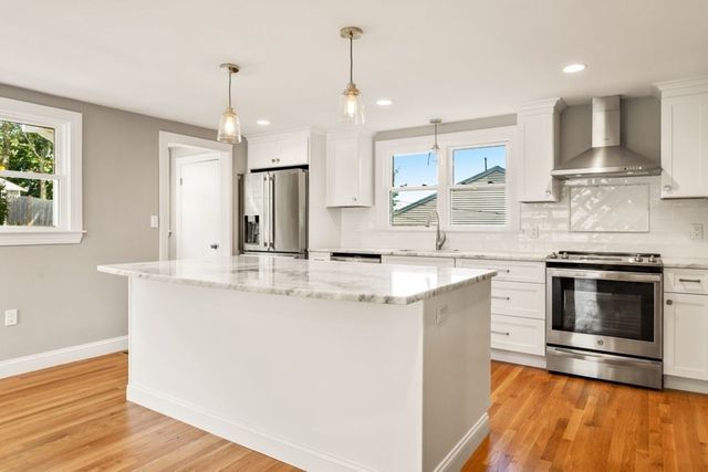a kitchen with stainless steel appliances granite countertop a sink a stove a refrigerator and island with wooden floor