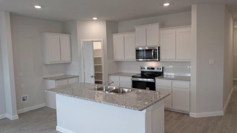 a kitchen with granite countertop a sink and a stove top oven with white cabinets