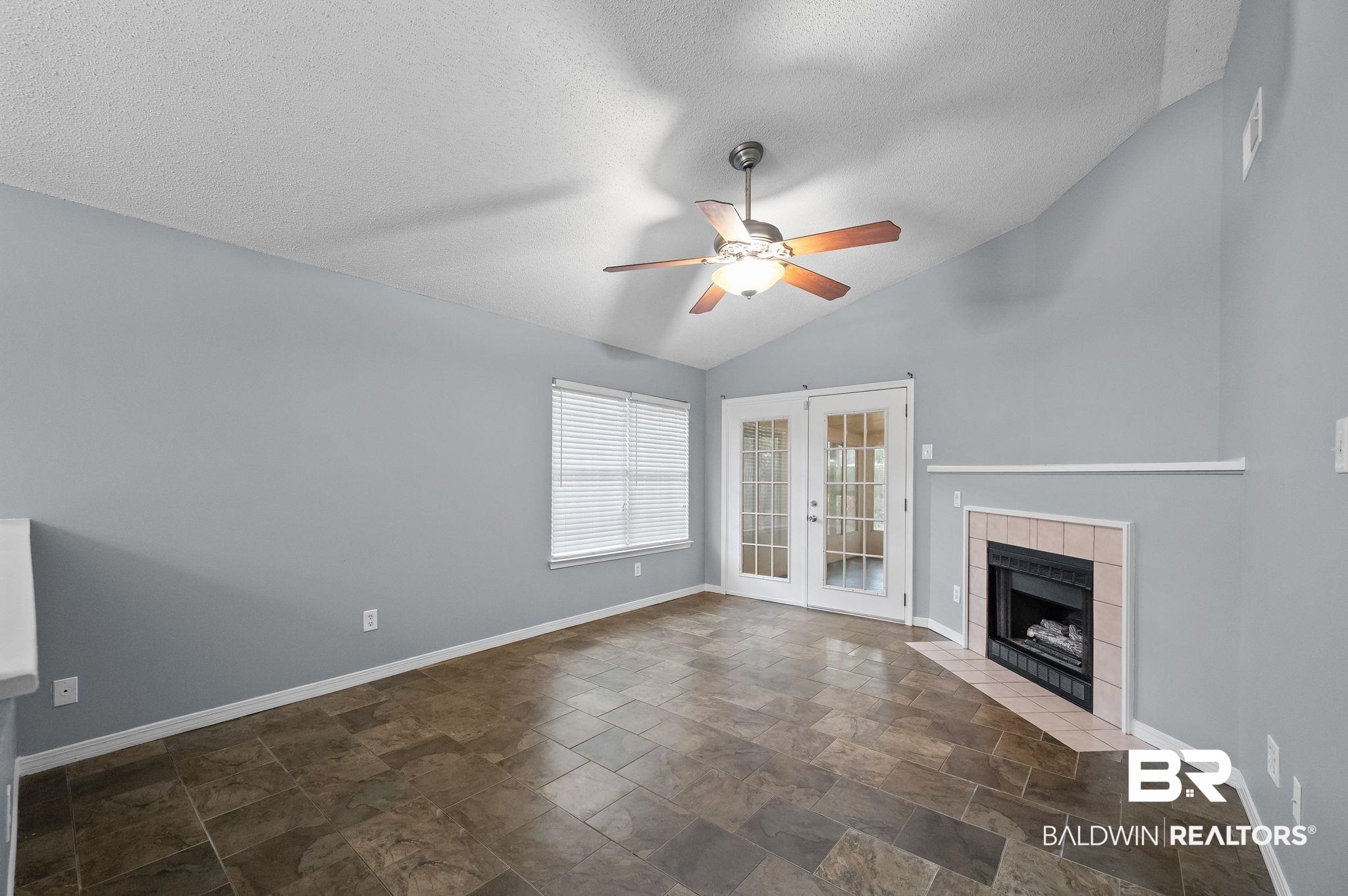 3744 Pepper Ridge Drive Mobile, AL 36693 - Photo 6 of 29 Unfurnished living room featuring french doors, a textured ceiling, a fireplace, stone finish flooring, and a ceiling fan