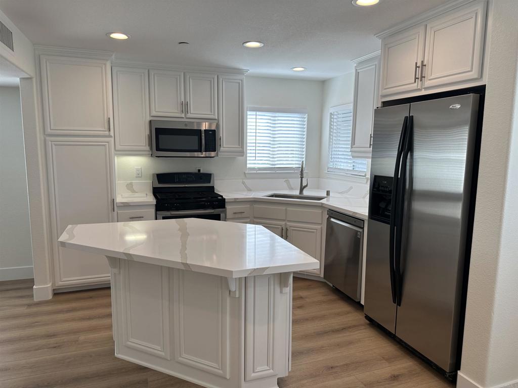 4026 Aidan Circle Carlsbad, CA 92008 - Photo 3 of 26 a kitchen with kitchen island white cabinets appliances and wooden floor