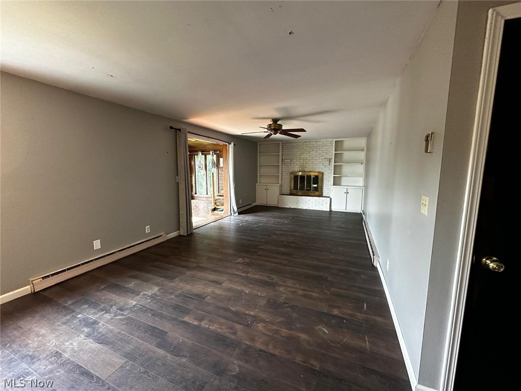 2093 Cambridge Road Coshocton, OH 43812 - Photo 12 of 32 Unfurnished living room with ceiling fan, built in features, dark hardwood / wood-style floors, a baseboard radiator, and a brick fireplace
