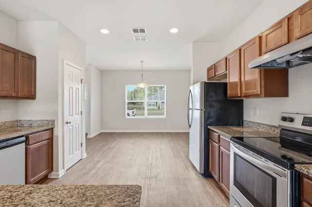 a kitchen with stainless steel appliances granite countertop a stove top oven a sink dishwasher a refrigerator and a dining table with wooden floor