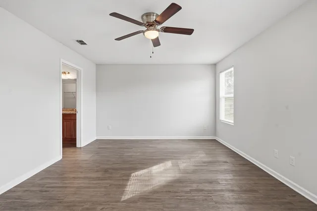 an empty room with wooden floor ceiling fan and windows