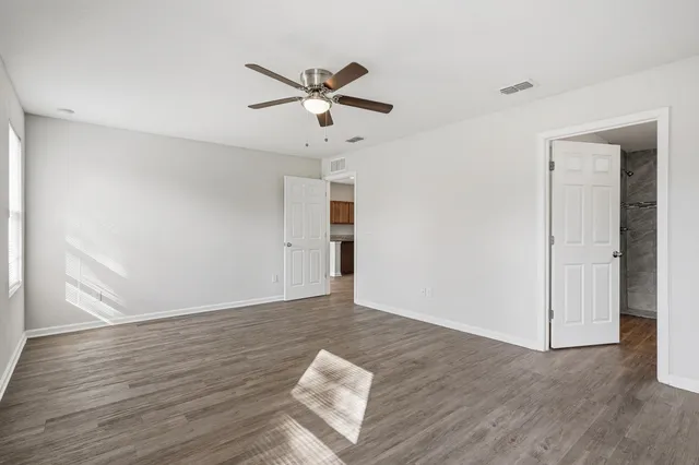 a view of an empty room with wooden floor and a ceiling fan