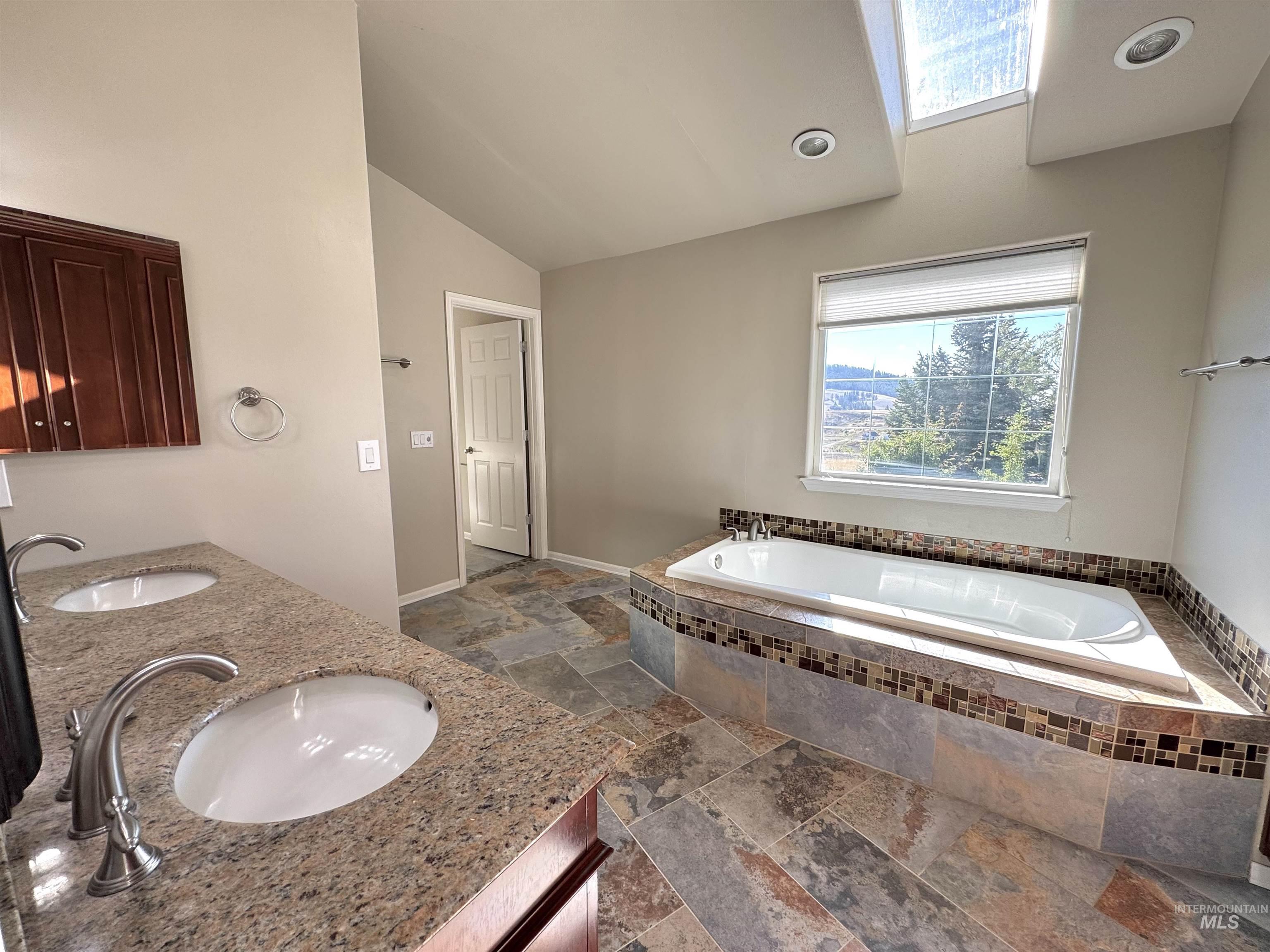 1030 Reams Road Moscow, ID 83843 - Photo 20 of 50 Full bathroom with a garden tub, stone tile flooring, vaulted ceiling, and double vanity