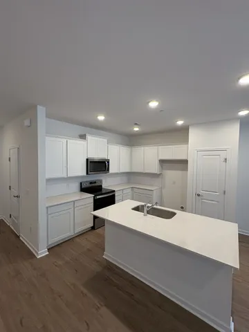 a kitchen with a sink a stove a refrigerator and white cabinets with wooden floor