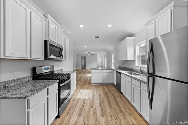 a large kitchen with a stove a sink dishwasher a refrigerator and white cabinets with wooden floor