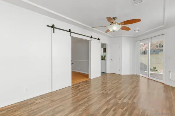 a view of an empty room with wooden floor and a ceiling fan
