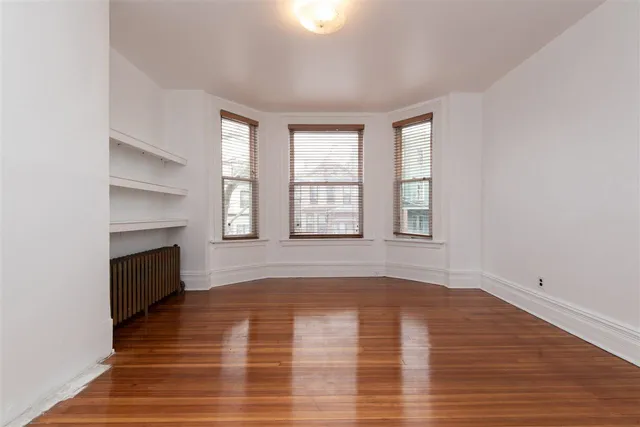 a view of an empty room with wooden floor fireplace and a window
