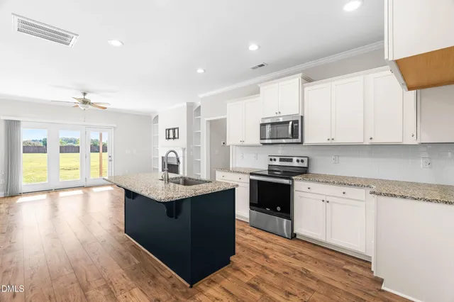 a kitchen with stainless steel appliances granite countertop a stove top oven a sink dishwasher a refrigerator and a dining table with wooden floor
