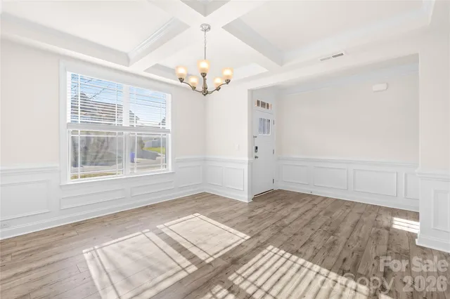 an empty room with wooden floor chandelier and windows