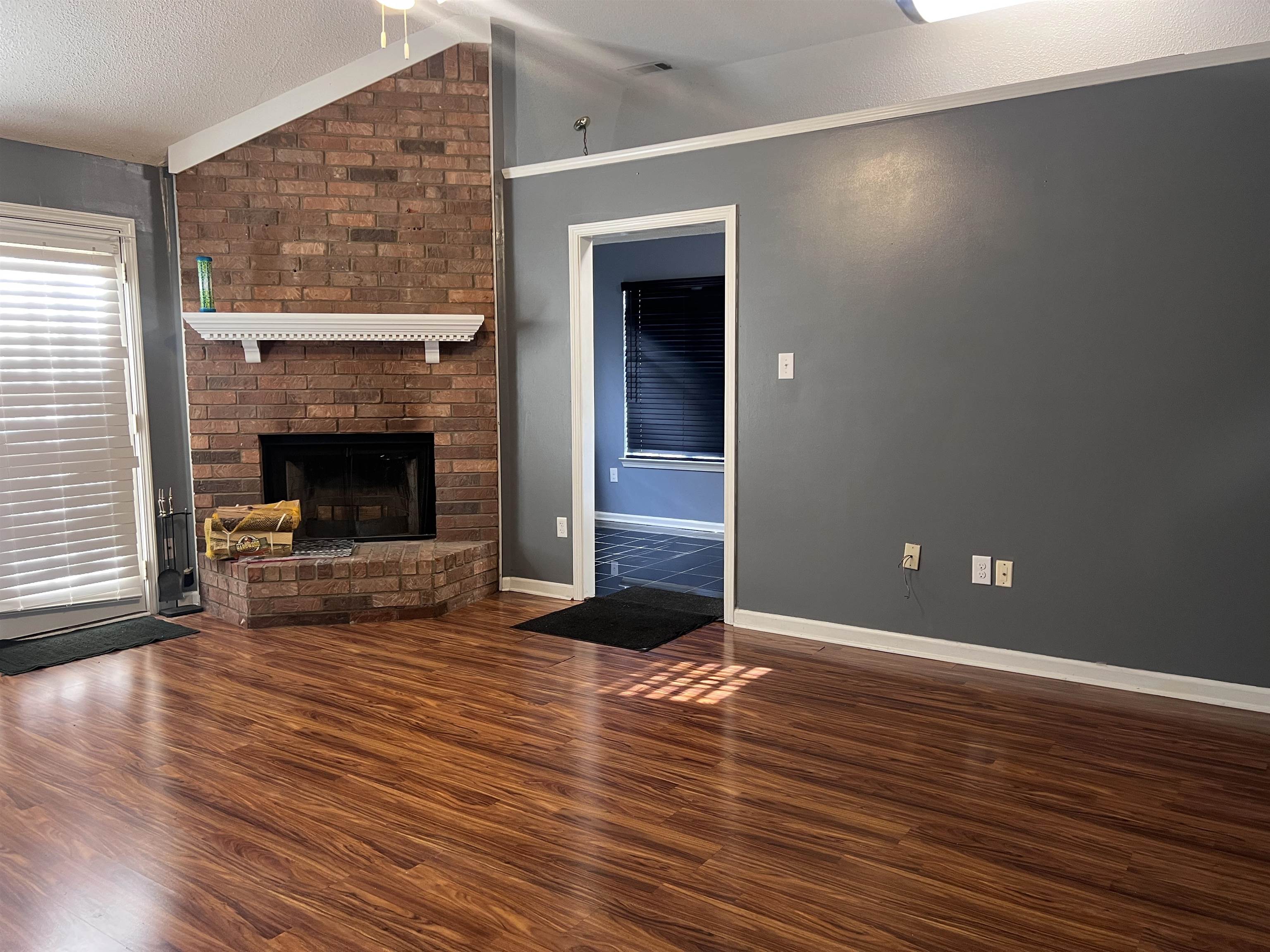 4005 Long Creek Road Memphis, TN 38125 - Photo 9 of 36 Warm wood-finish flooring, brick fireplace with a white mantle, vaulted ceiling with a ceiling fan, and painted walls