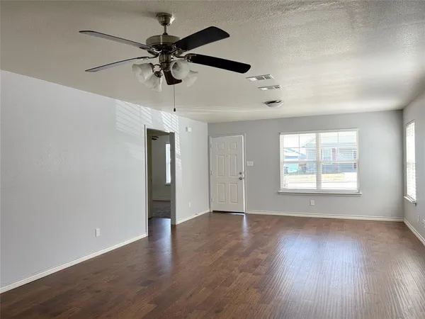 an empty room with wooden floor ceiling fan and windows