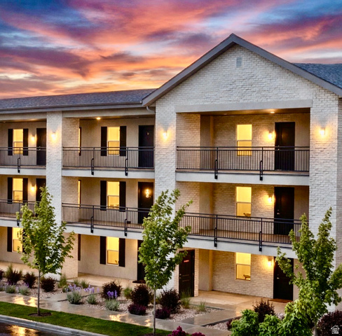 Multi-story building featuring light-colored brick veneer, black railing balconies, and individual entry doors