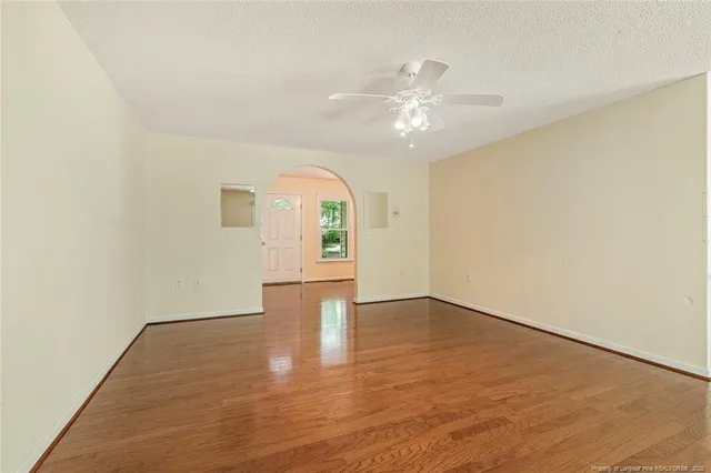 an empty room with wooden floor fan and windows