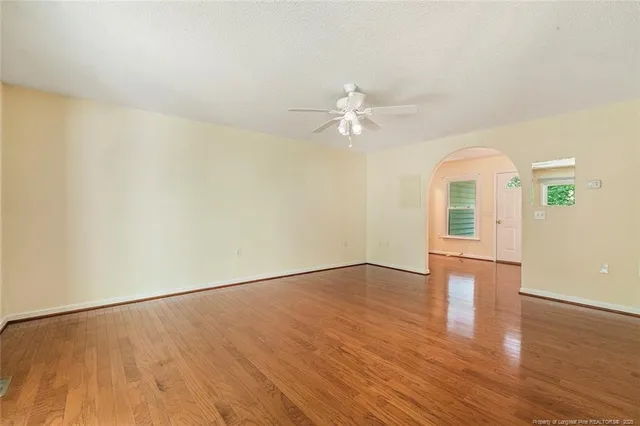 an empty room with wooden floor chandelier fan and windows