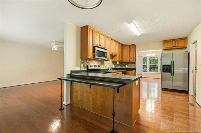 a kitchen with stainless steel appliances granite countertop a refrigerator a stove a sink and a microwave oven with wooden floor