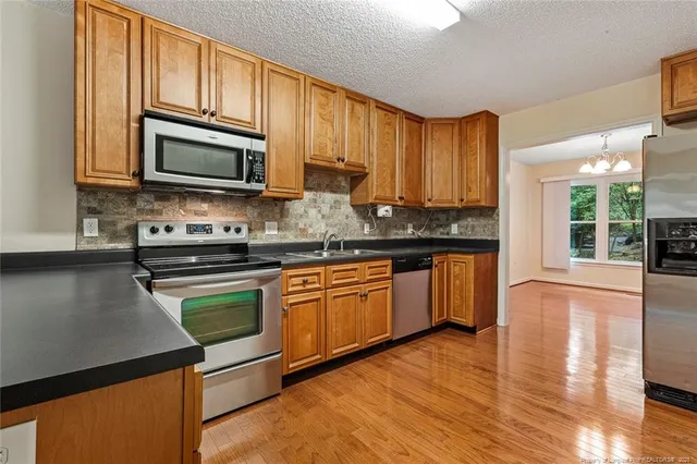 a kitchen with stainless steel appliances granite countertop wooden cabinets a stove top oven a sink and dishwasher with wooden floor