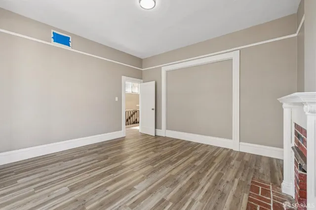 a view of an empty room with wooden floor fireplace and a window