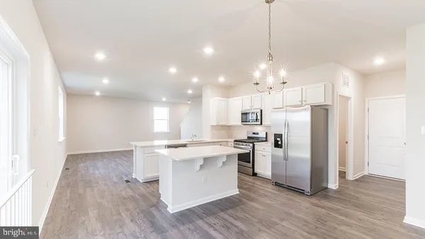a kitchen with stainless steel appliances granite countertop a refrigerator a sink dishwasher a stove and white cabinets with wooden floor