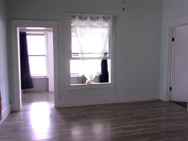 an empty room with wooden floor chandelier and windows