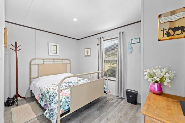 a bedroom with a bed potted plant on the dresser and a wooden floor