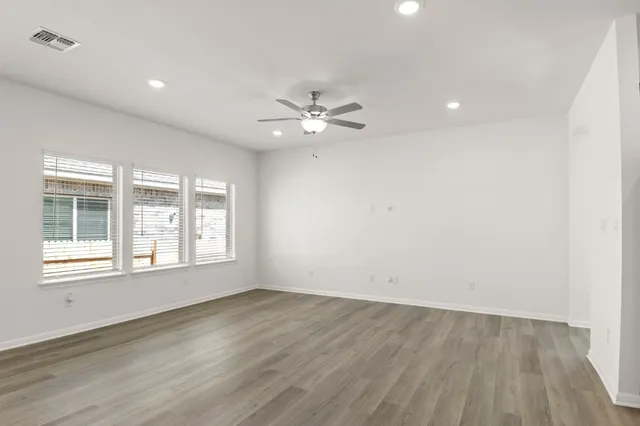 an empty room with wooden floor and windows with curtains