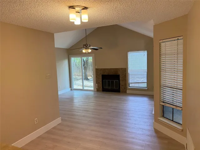 an empty room with wooden floor fireplace and windows