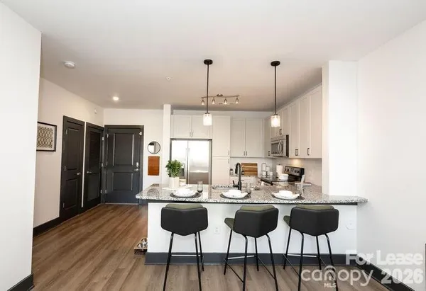 a kitchen with stainless steel appliances kitchen island granite countertop a dining table chairs and a refrigerator