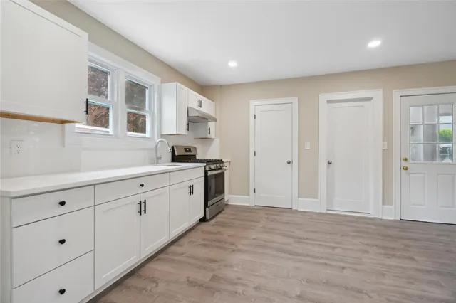 a large white kitchen with granite countertop a sink and dishwasher with wooden floor