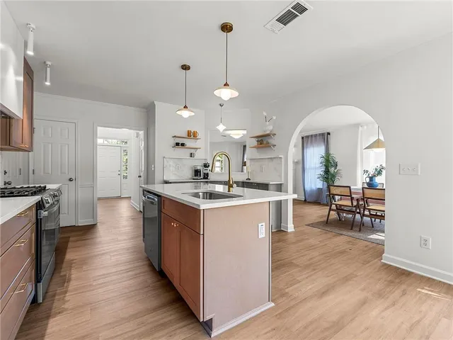 a large kitchen with granite countertop a large center island a sink dishwasher a stove and a dining table with wooden floor