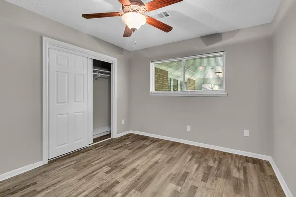 an empty room with wooden floor chandelier fan and windows