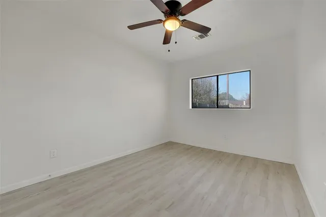 an empty room with wooden floor ceiling fan and window