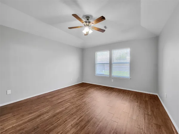 an empty room with wooden floor fan and windows