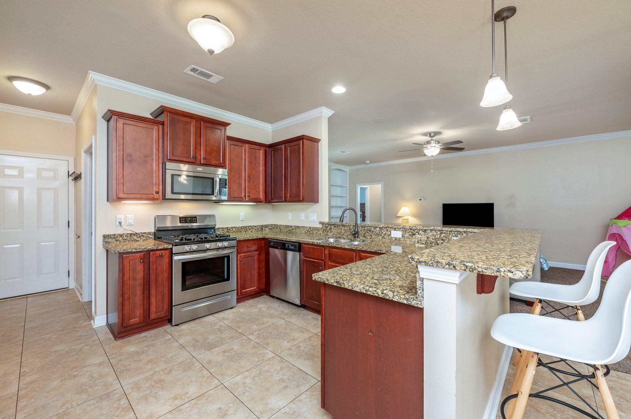 4615 Chanan Drive Crestview, FL 32539 - Photo 17 of 47 a large kitchen with stainless steel appliances granite countertop a stove top oven a sink dishwasher a dining table and chairs with wooden floor