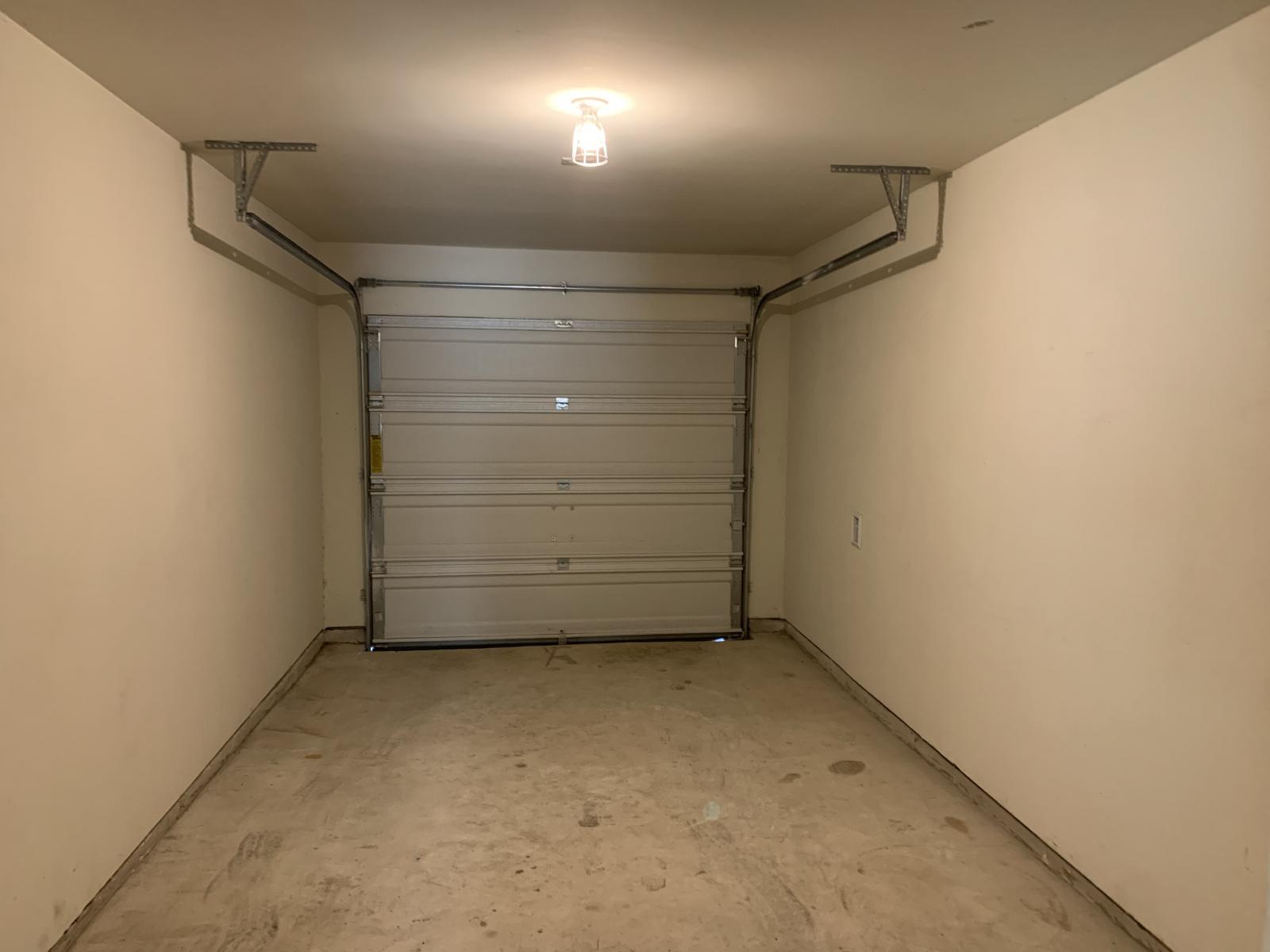217 Denson Lane Jarrell, TX 76537 - Photo 7 of 26 Single-car garage featuring a sectional overhead door, concrete flooring, painted walls, and an overhead light fixture