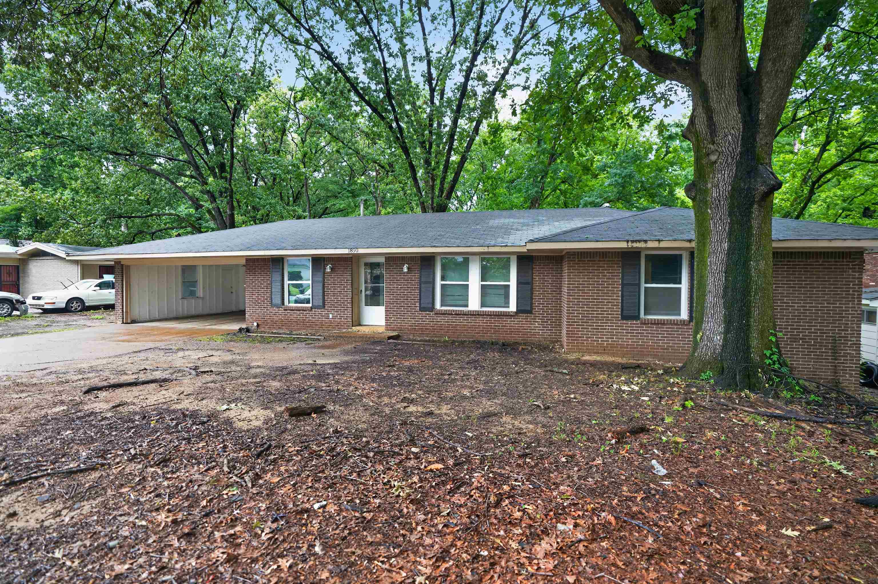Brick ranch-style residence featuring a dark shingle roof, white-framed windows with dark shutters, and a covered carport