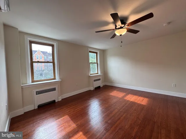 an empty room with wooden floor fan and windows