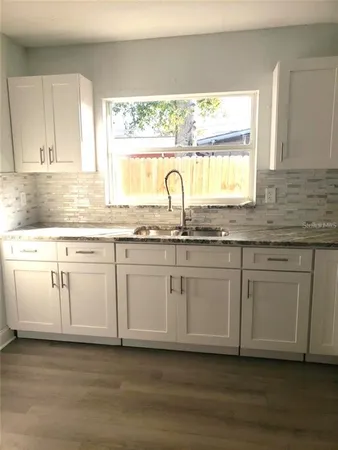 a white kitchen with granite countertop white cabinets and a large window