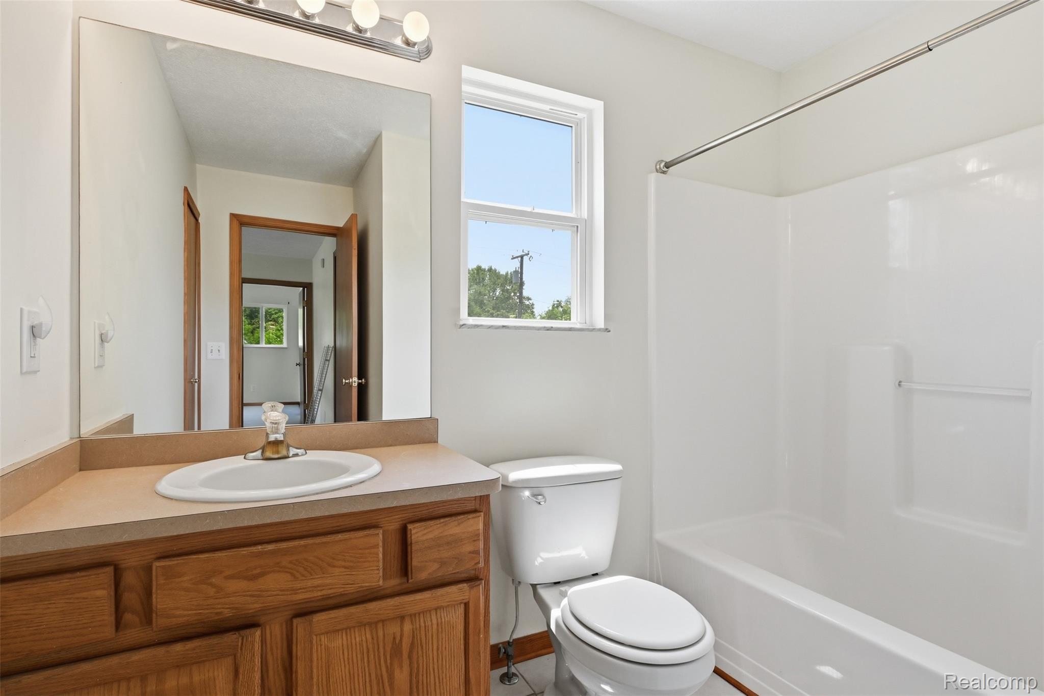4482 Pleasant Valley Road Brighton, MI 48114 - Photo 16 of 35 Bathroom featuring a wood-finish vanity with an integrated sink, a large wall-mounted mirror, overhead vanity lighting, a window, and a white fiberglass tub with a shower surround