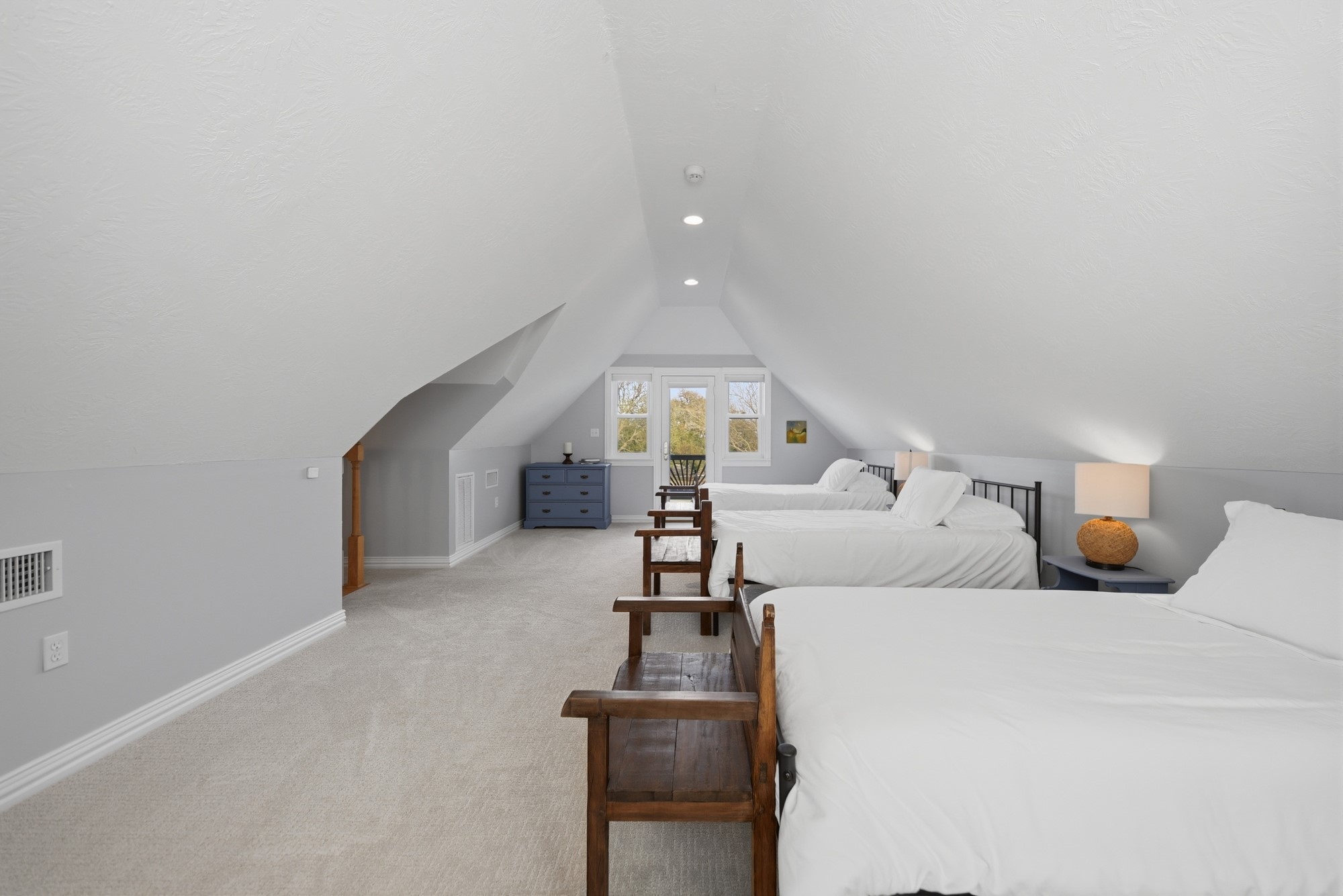 5255 Ganske Road Burton, TX 77835 - Photo 14 of 46 Spacious loft bedroom with a vaulted ceiling, featuring two beds and ample natural light from the window. The room is carpeted, with neutral tones and cozy lighting, offering a peaceful retreat.