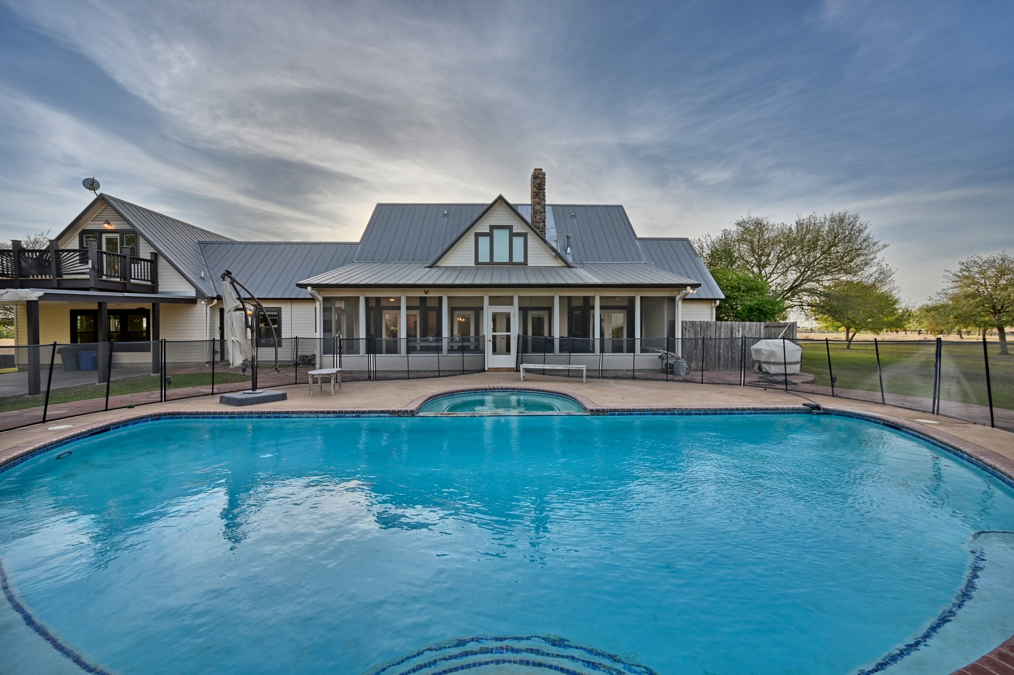 5255 Ganske Road Burton, TX 77835 - Photo 16 of 46 Large swimming pool. The house has a modern farmhouse style with a metal roof and a screened porch, offering ample outdoor living space. The surroundings are open and scenic, providing a serene setting.