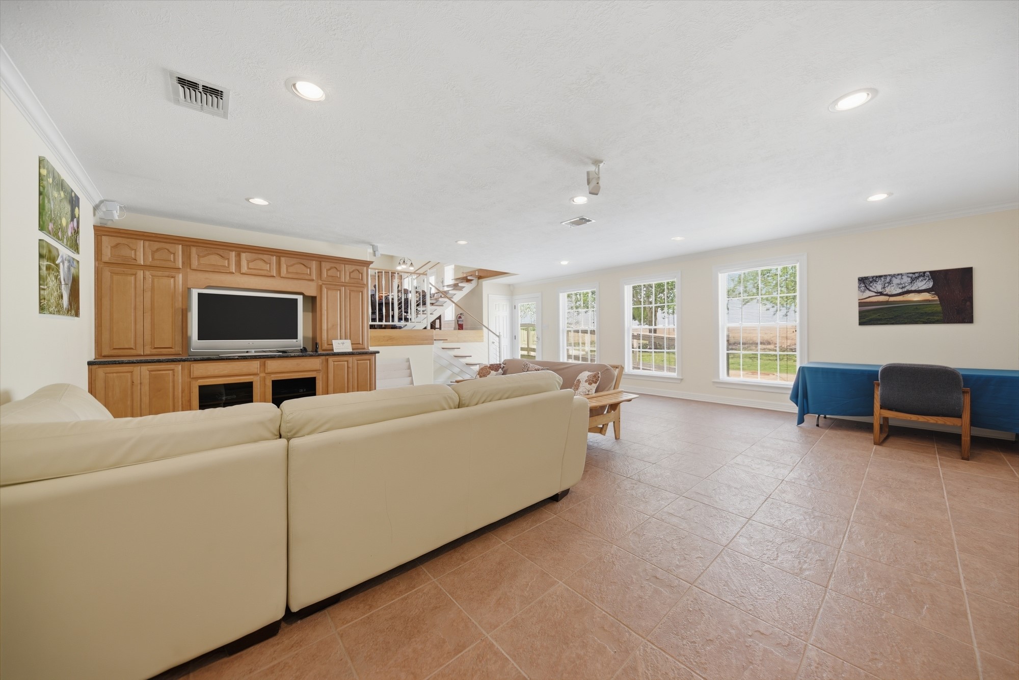 5255 Ganske Road Burton, TX 77835 - Photo 20 of 46 Spacious living room with large windows providing ample natural light. Features include tiled flooring, a built-in entertainment center, and a cozy seating area. Open staircase adds elegance to the space.
