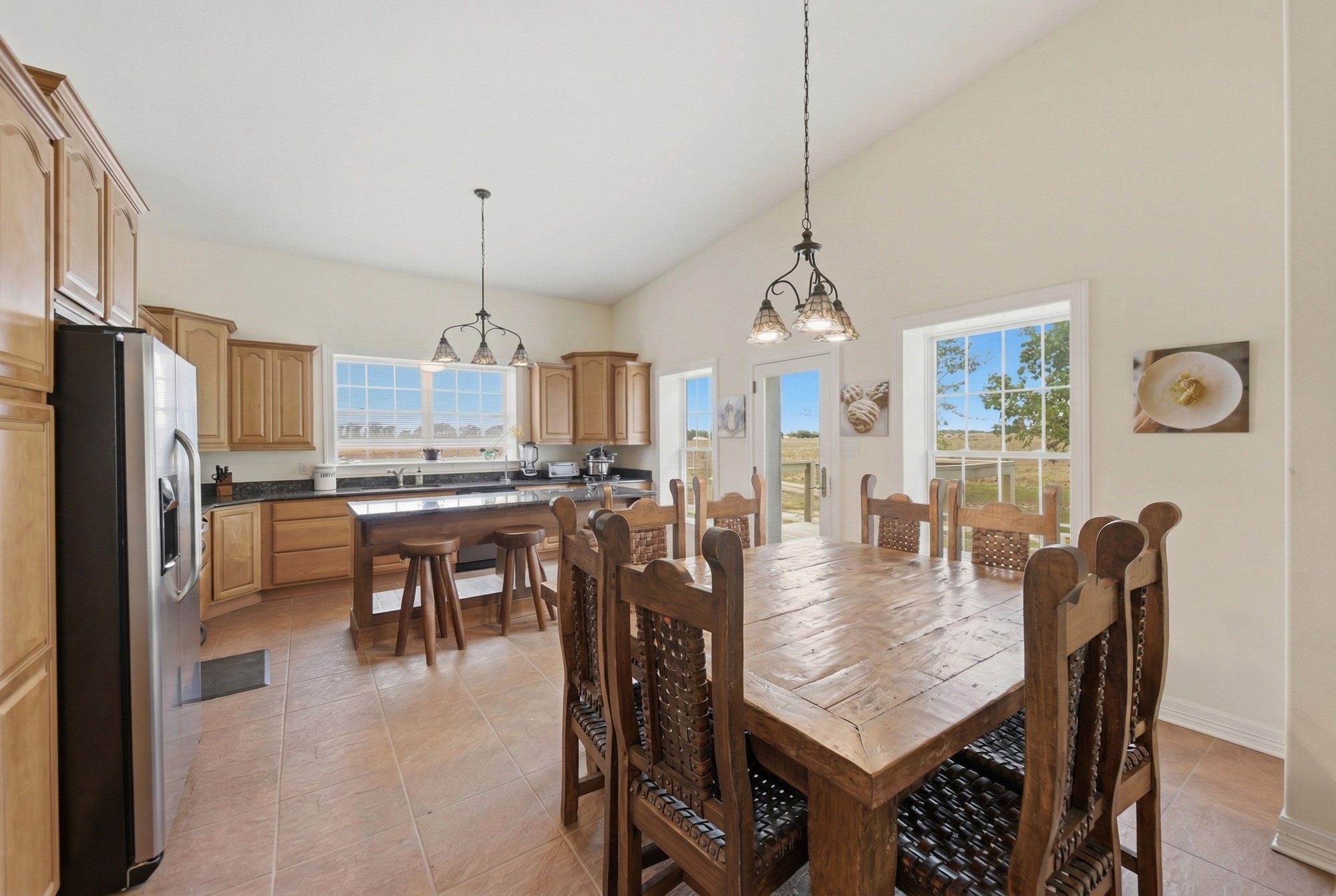 5255 Ganske Road Burton, TX 77835 - Photo 21 of 46 This inviting kitchen-dining area features high ceilings, natural light, and rustic charm. It includes wooden cabinetry, a large farmhouse dining table, and a central island with seating. The room opens to outdoor views, creating a cozy yet spacious environment perfect for family gatherings.